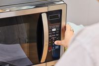 A thumb pressing a button on the Farberware Countertop Compact Microwave (FMWO11AHTBKB) 