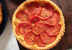 Tomato tart with layered tomato slices on top of a golden crust placed on a wooden surface