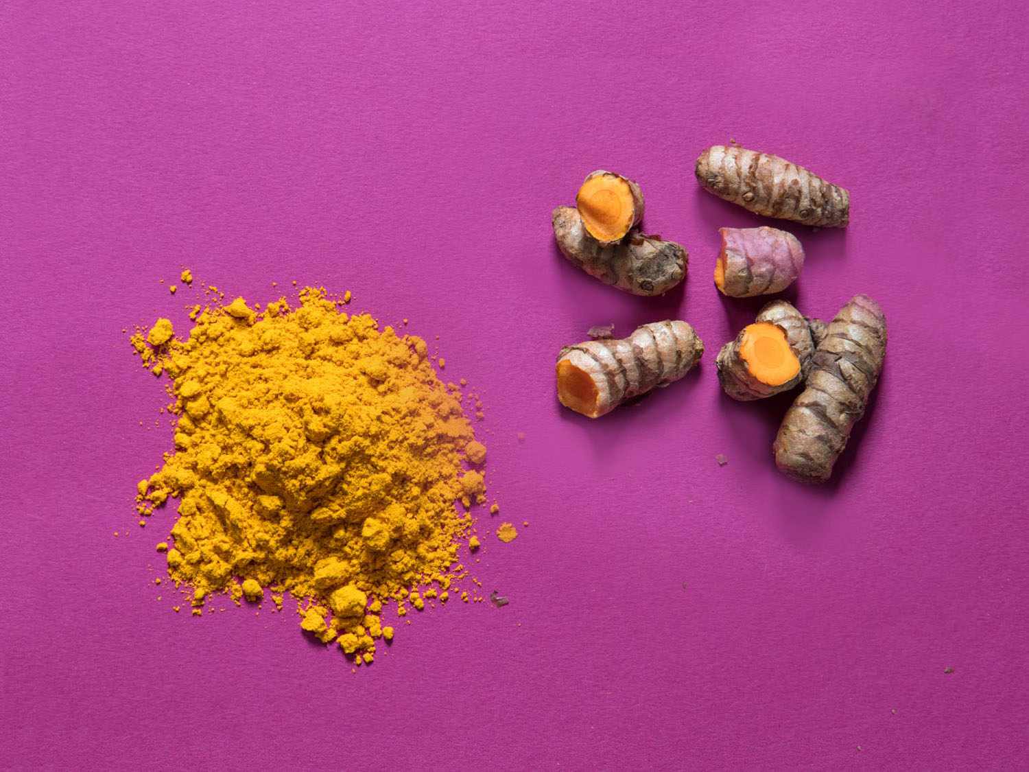 Closeup of dried, ground turmeric and fresh turmeric root.