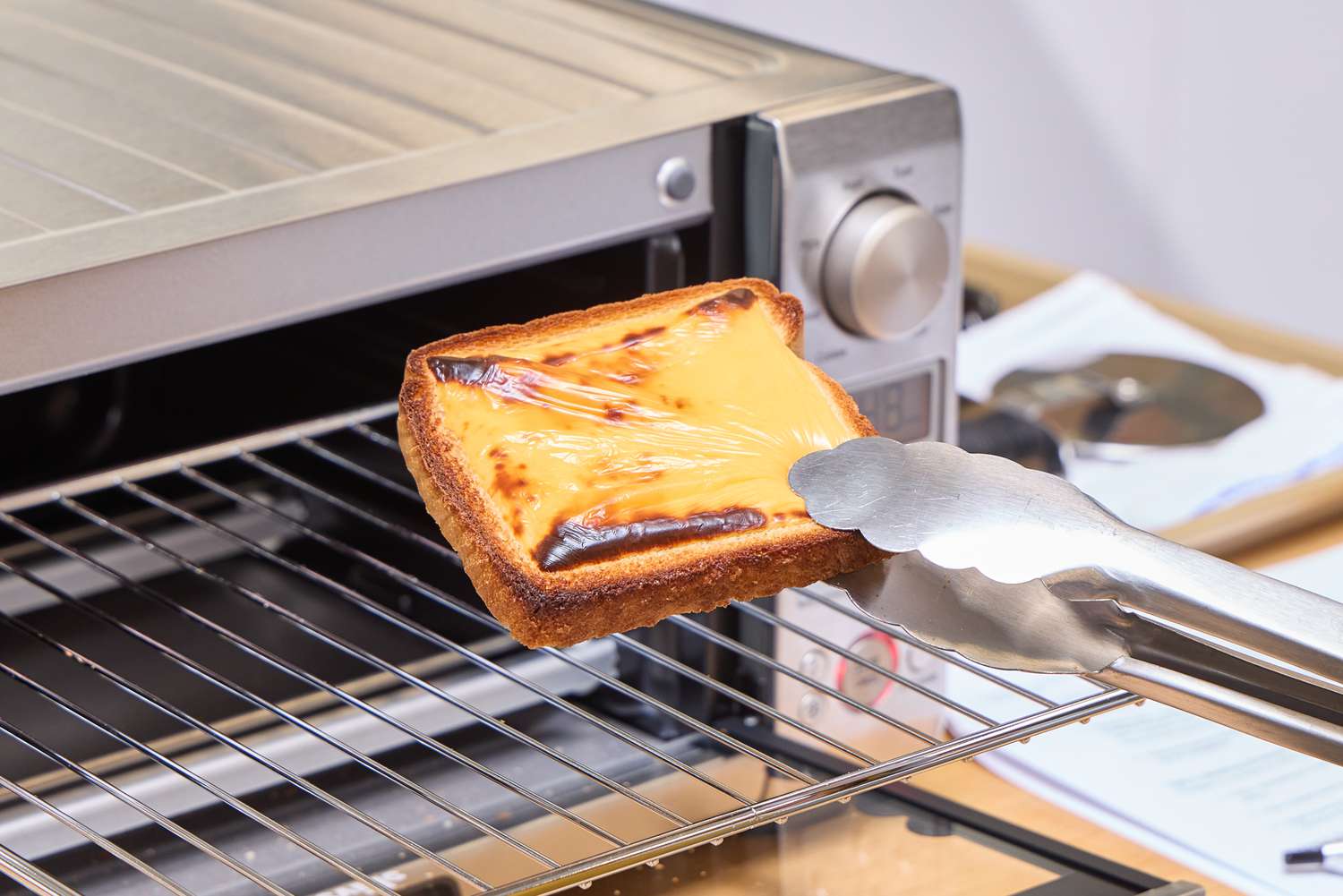 Tongs lifting cheese toast from the Breville the Mini Smart Oven BOV450XL