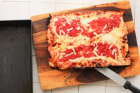 A pizza made in the LloydPans Kitchenware 10 by 14 Inch Detroit Style Pizza Pan on a cutting board