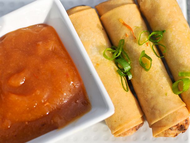 Three egg rolls lying next to a small square bowl of duck sauce.