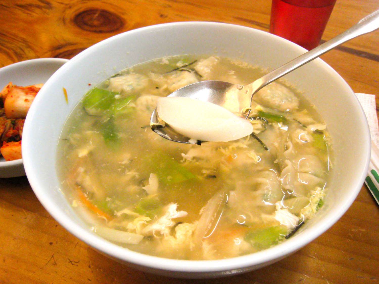 spooning a piece of rice cake from a bowl of dduk guk