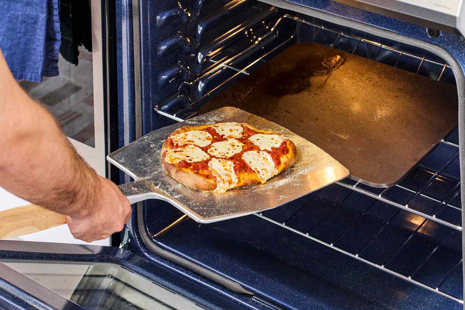 A person using a pizza peel to remove a cooked pizza from a baking steel.