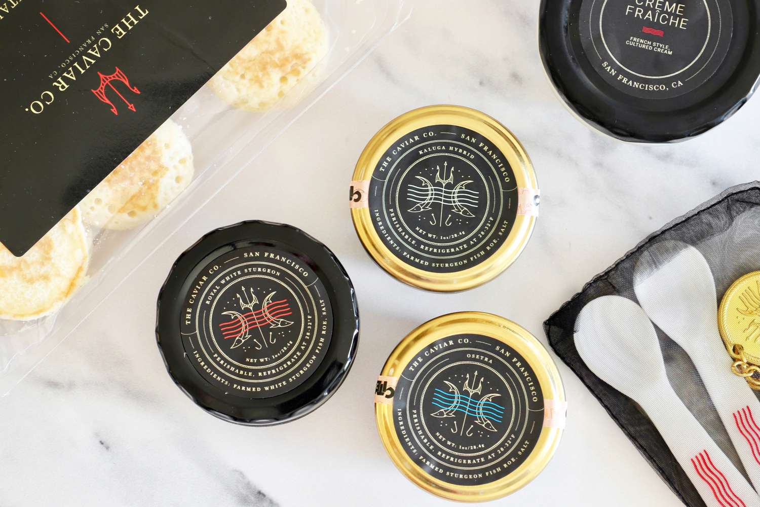 A collection of Caviar Co products: crème fraîche, mother-of-pearl spoons, a caviar key, prepared blinis, royal white sturgeon caviar, osetra caviar, and kaluga hybrid caviar