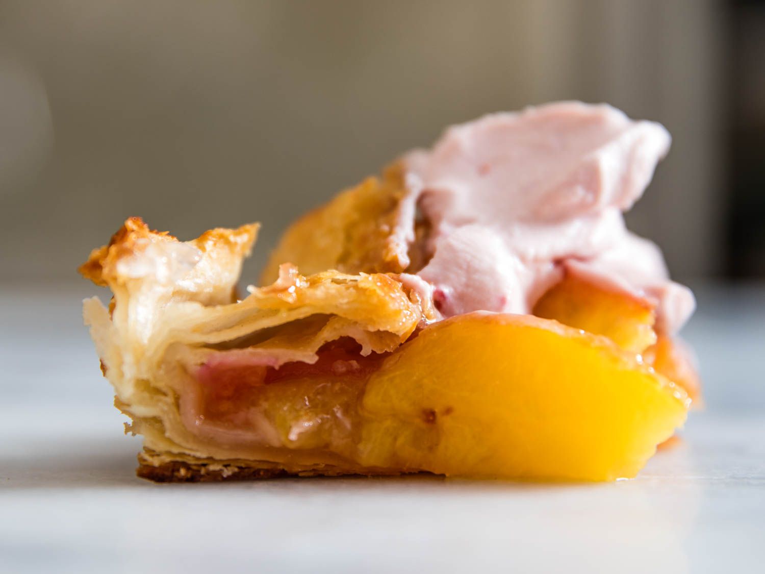 Profile closeup of a slice of peach galette, showing the layers of flaky dough and tender fruit.