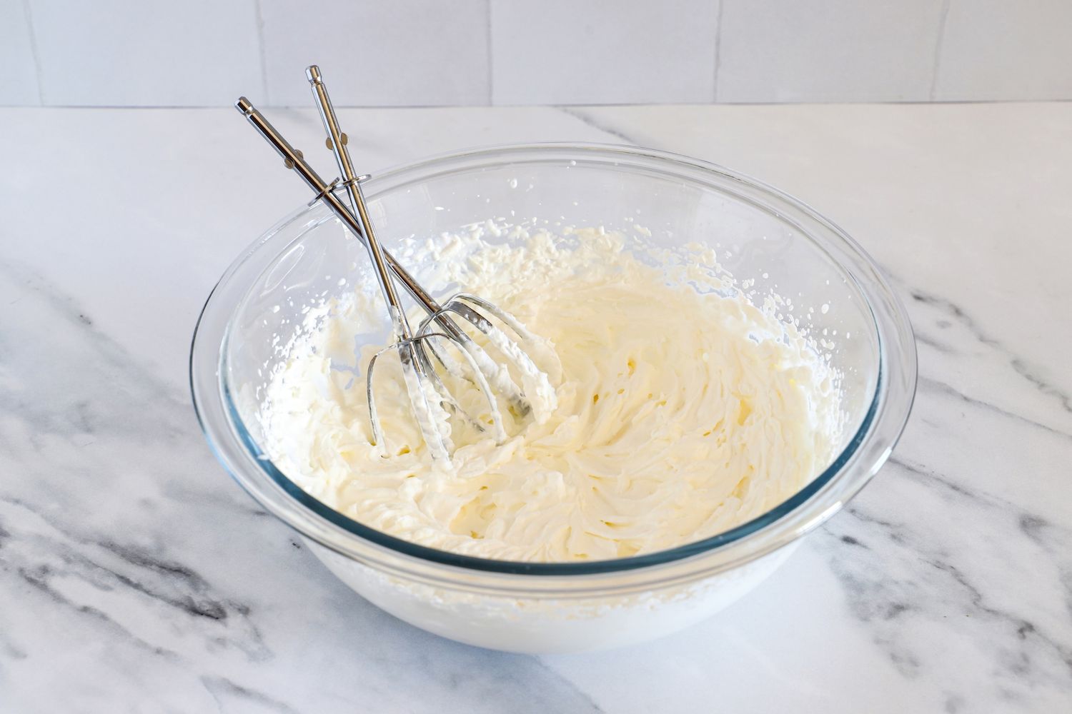 A Pyrex mixing bowl containing whipped cream with a pair of beaters resting inside