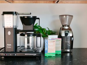 A coffee maker sitting next to two packages of descaler and cleaner and a burr grinder