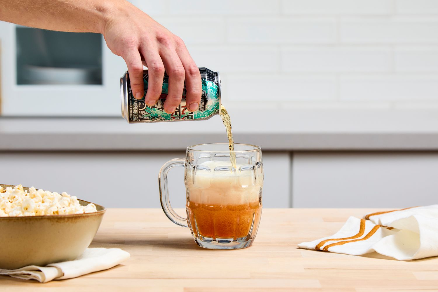 A person pouring beer into a dimpled pint glass.
