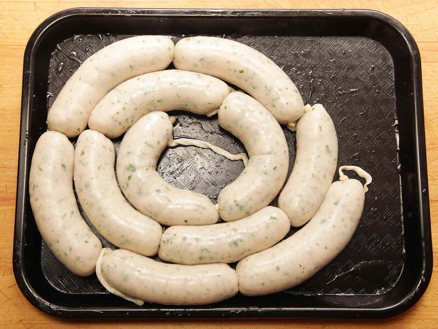 A black tray full of weisswurst links, coiled into a spiral.