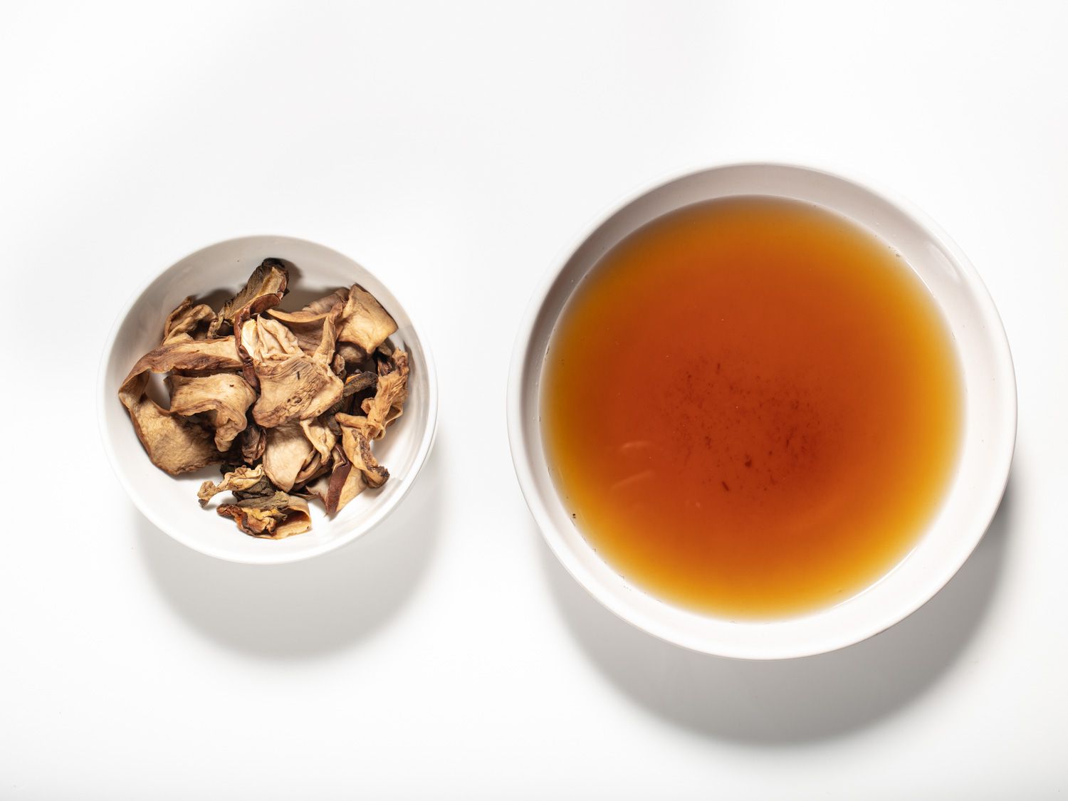 One small bowl holding rehydrated dried mushrooms and a larger bowl holding the mushroom soaking liquid.