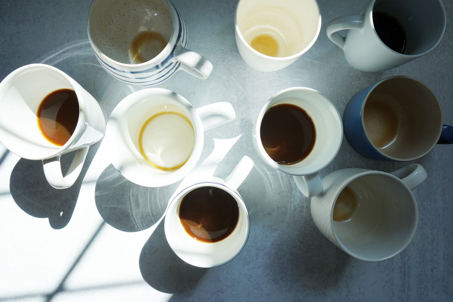 Several coffee mugs on a grey surface with varying amounts of coffee