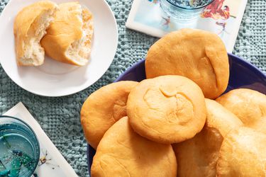 Overhead angle of Platter of Johnny Cakes on a blue platter, with a cake on a smaller plate in front, ripped open. 2 glasses of sparkling water and blue tablecloth 