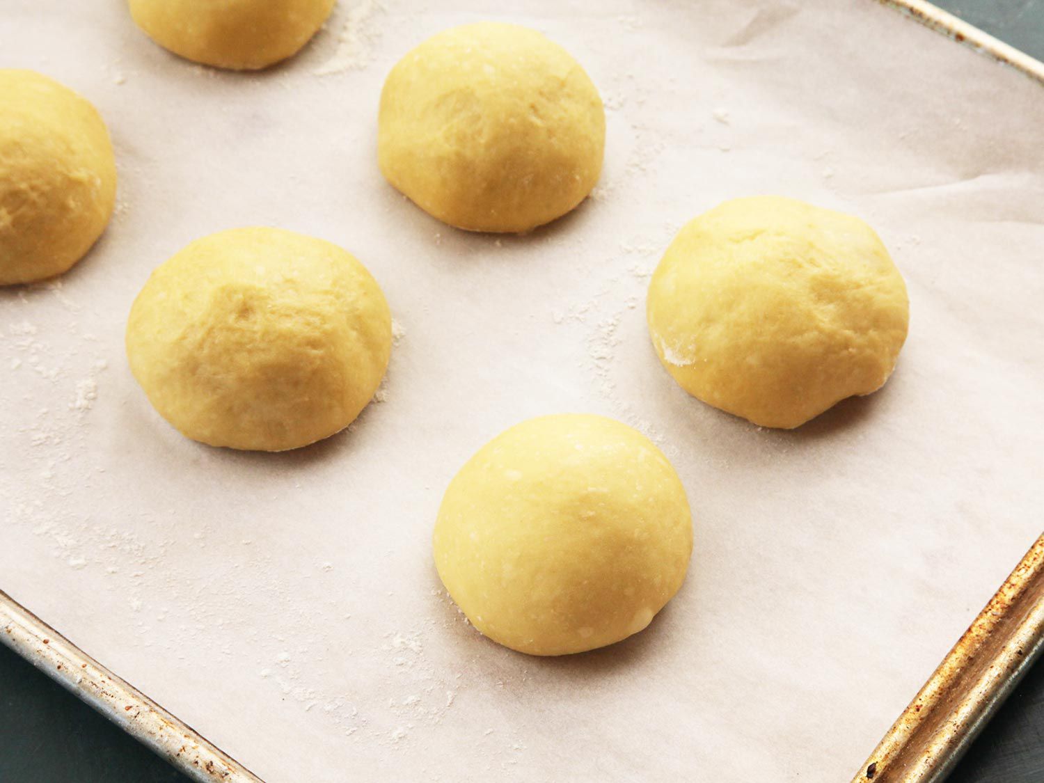 Closeup of the shaped portions of cemita dough, arranged on a parchment-lined baking sheet.