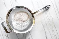 All-Clad Stainless-Steel Strainer, Set of 3 with flour on a light surface