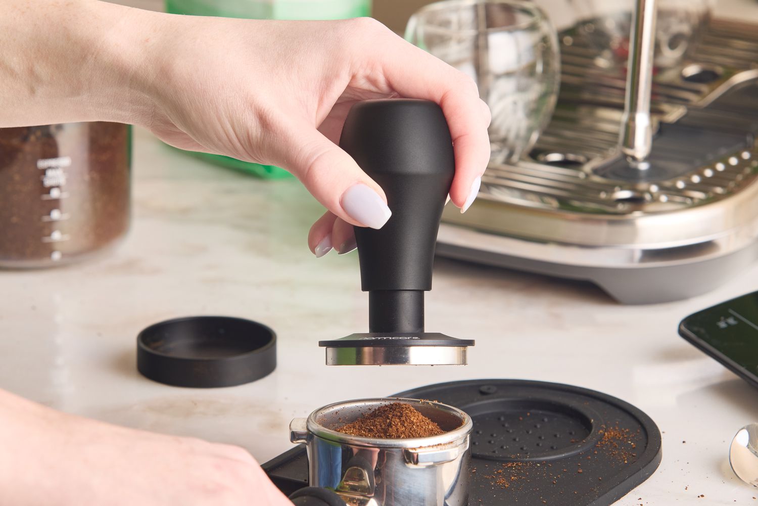 A person lowering an espresso tamper onto a bed of grounds in a portafilter.