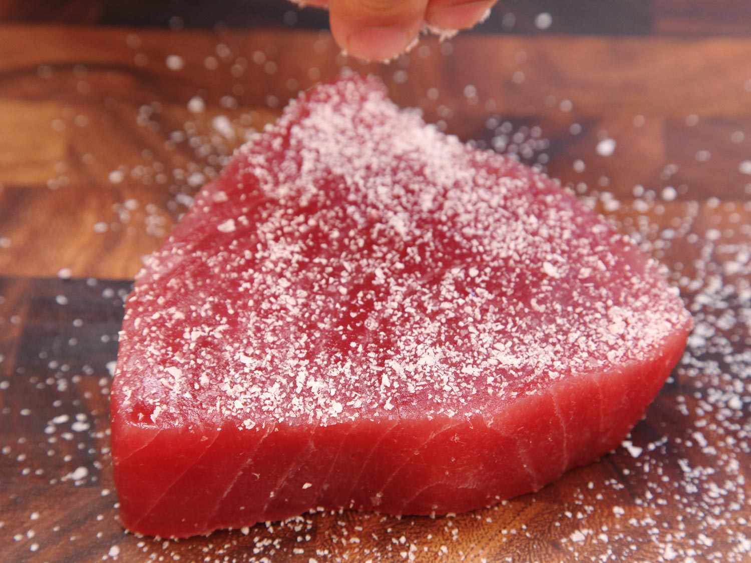 Author showering a raw tuna steak with salt.