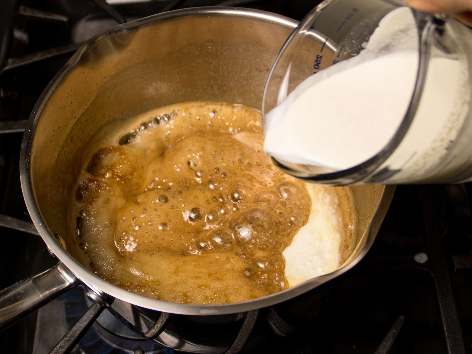 Cream being poured into the caramel in a saucepan on the stovetop.