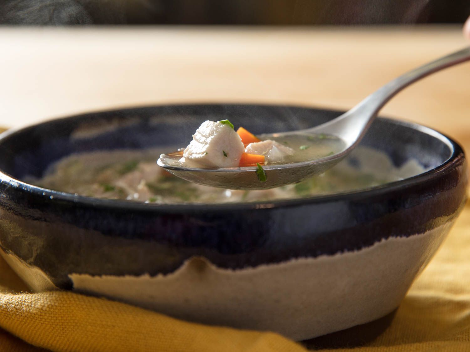 A spoonful of chicken soup being lifted out of a bowl.