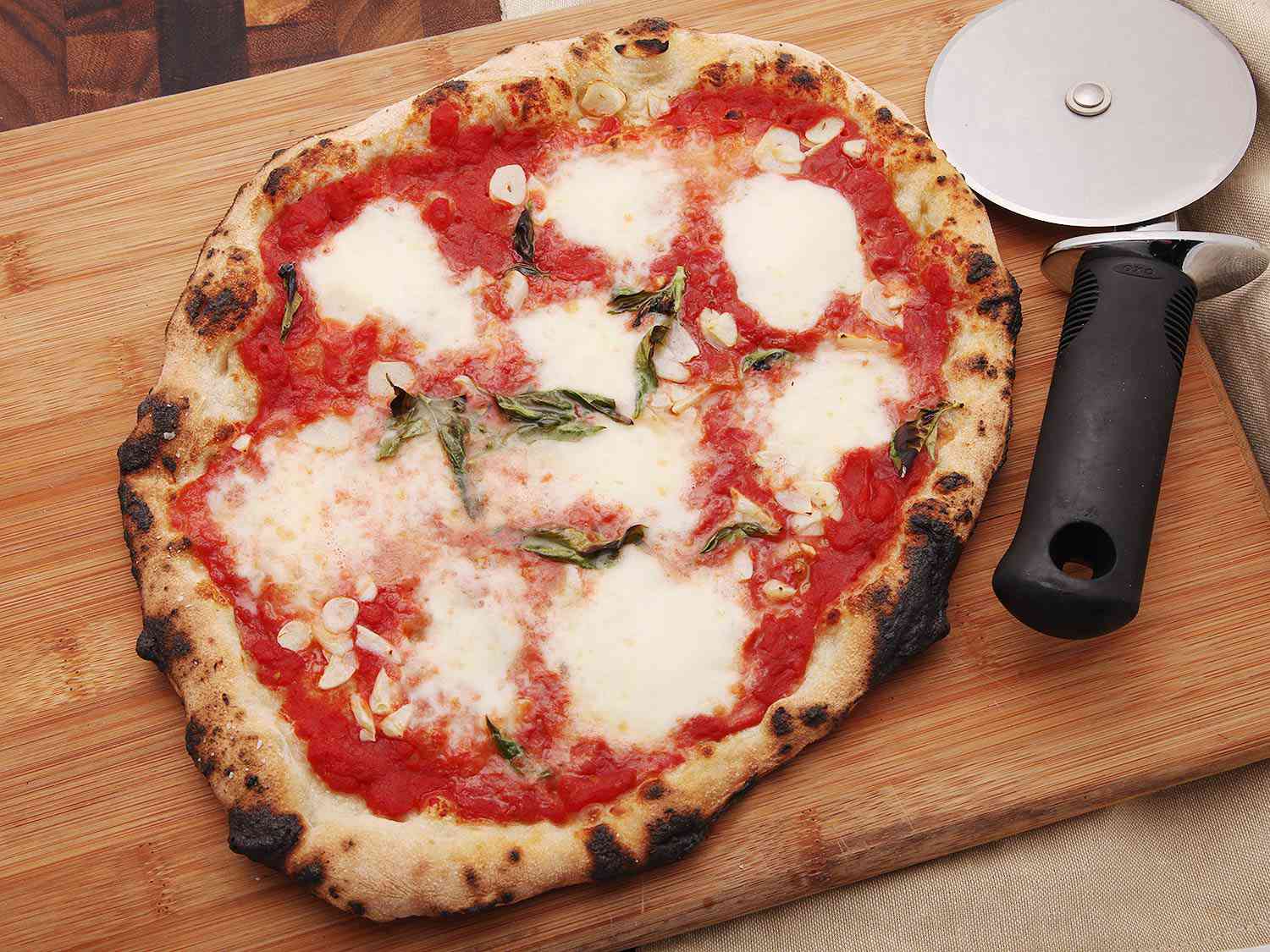 Charred margarita pizza on wooden cutting board with pizza wheel