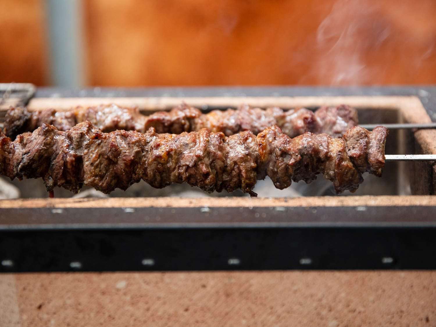 Side view of lamb skewers grilling over coals on a Japanese konro grill