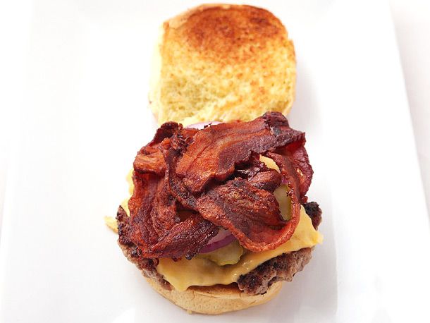 A cheeseburger assembled with three strips of bacon arranged on top. The bacon strips have been folded into triangles before being baked.