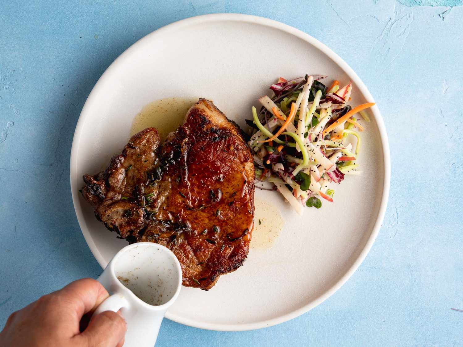 pouring hot drippings over pork chop on a plate with a side salad