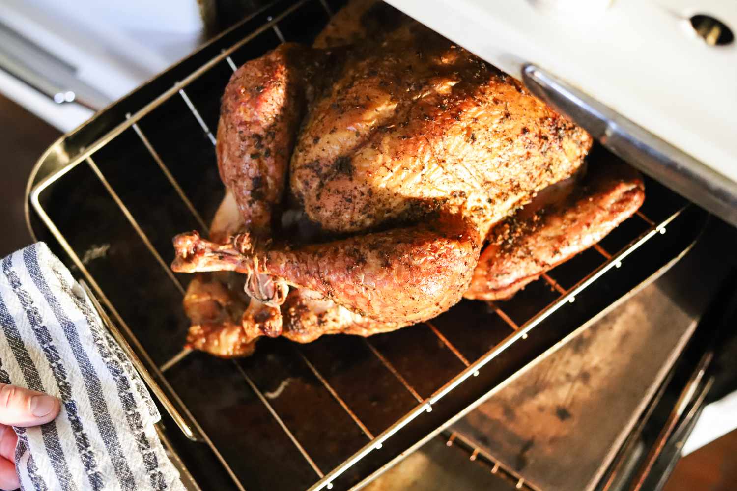 A person removing the Cuisinart roasting pan with a roasted chicken in it out for the oven.