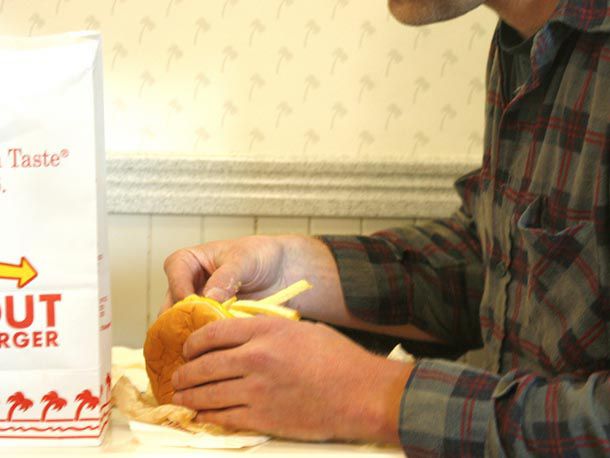 A man putting French fries into his In-N-Out burger