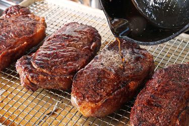 Hot pan drippings are poured on seared and rested steaks to "fat flash" them.