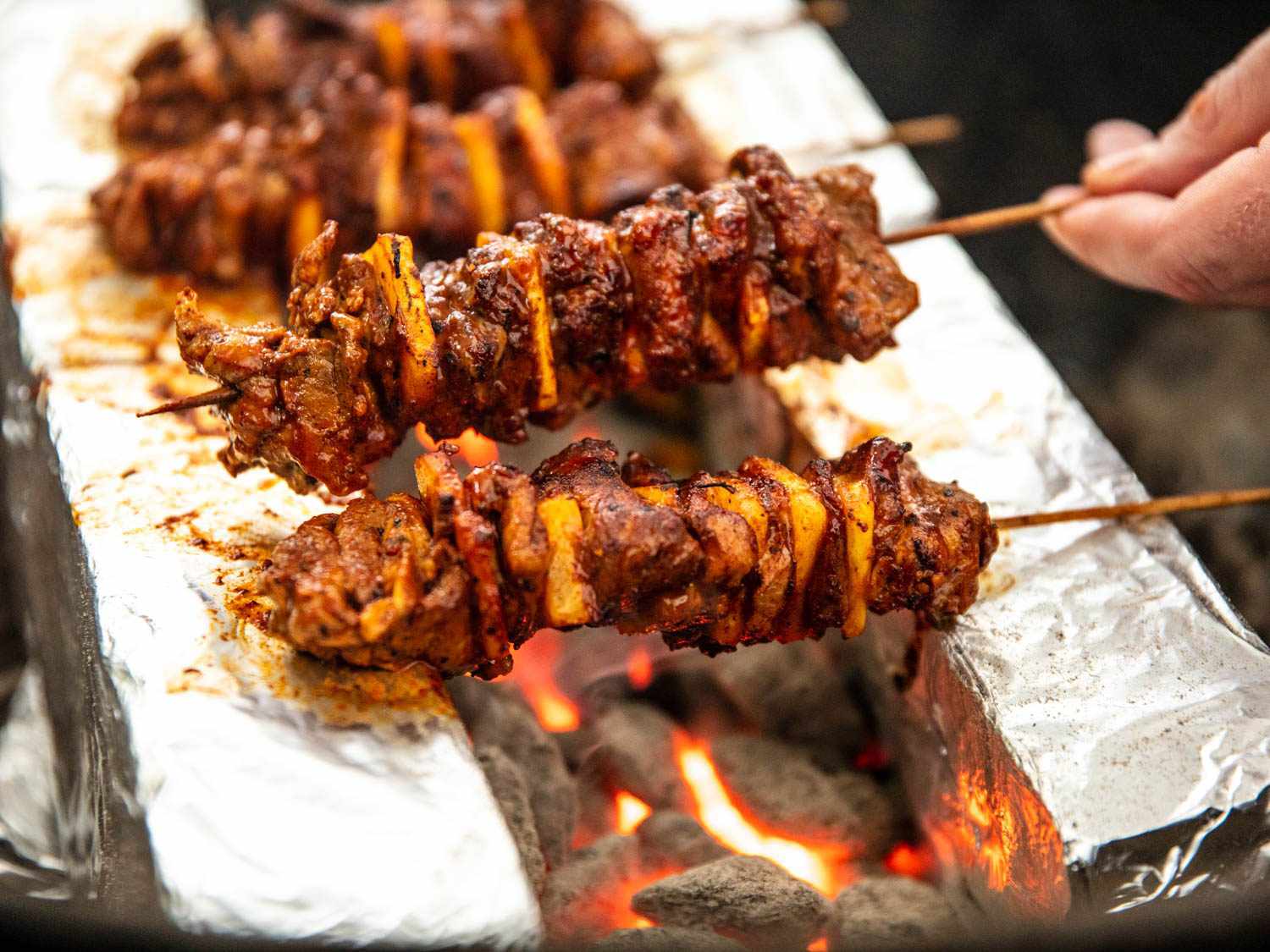 Turning al pastor skewers over hot coals
