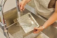 A person washing parts of the Lelit MaraX Espresso Machine PL62X-120 in a sink
