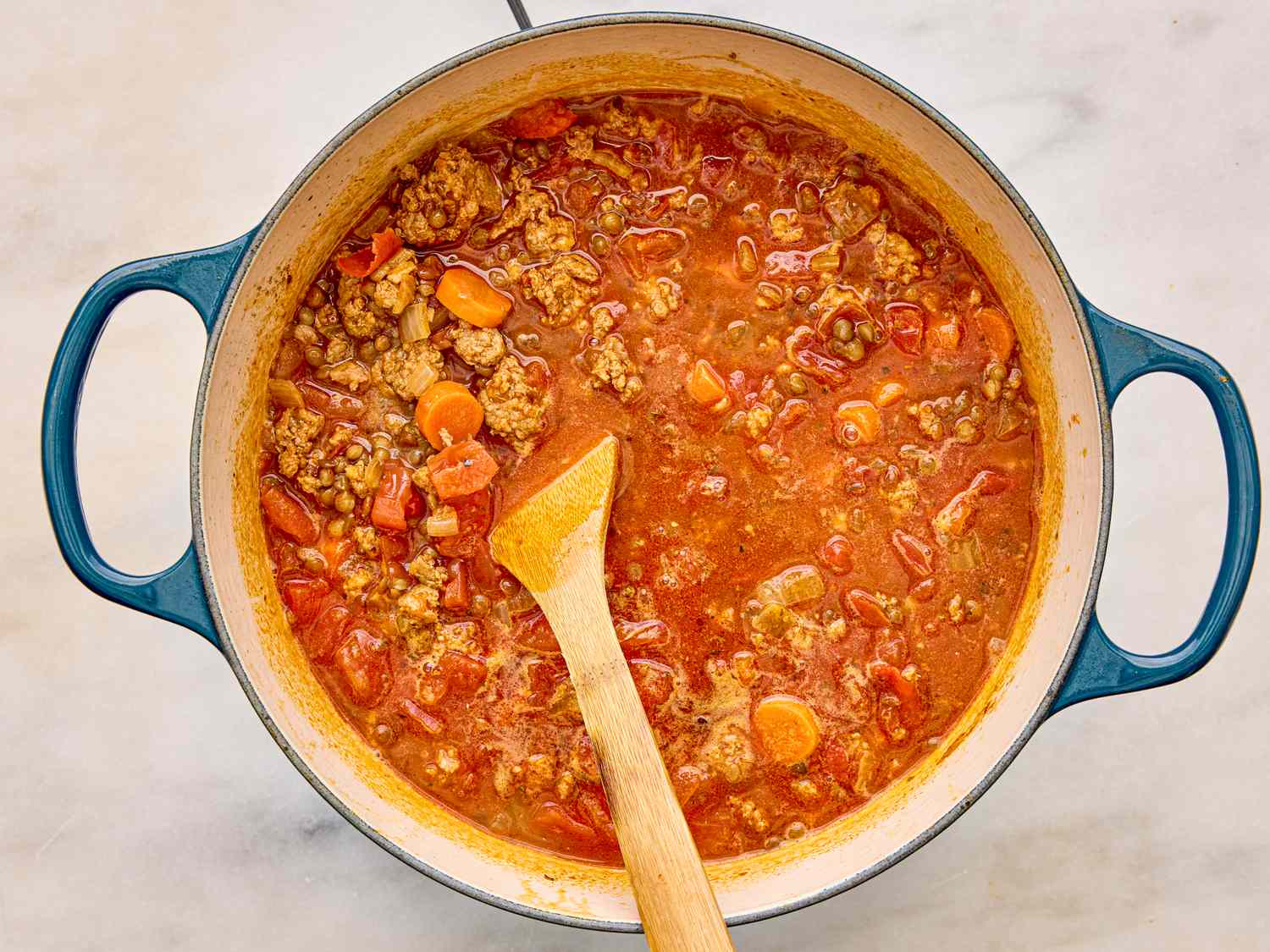 A pot of sausage and lentil soup with a wooden spoon resting in it