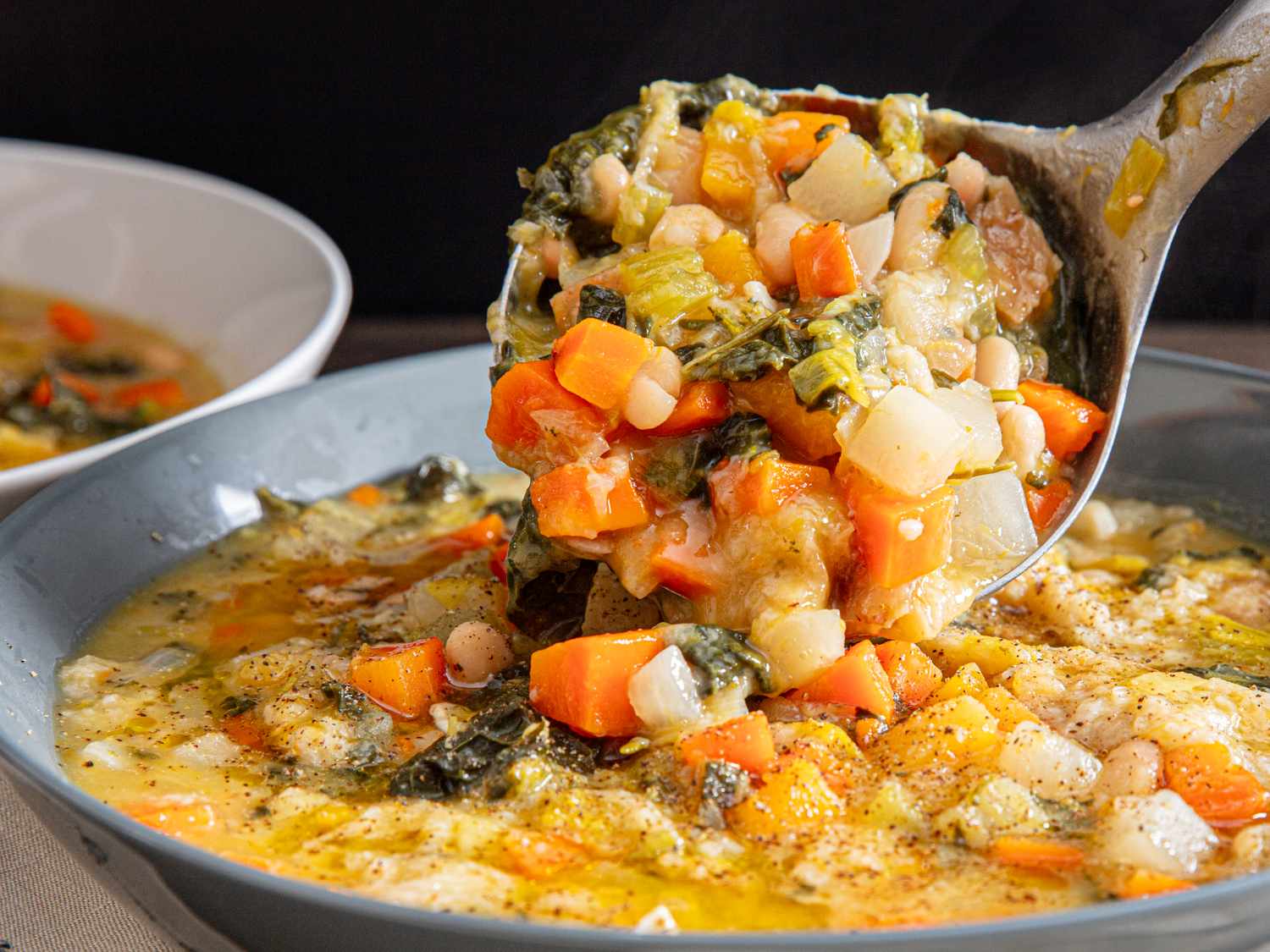 A ladle lifting thick and chunky vegetable soup from a bowl