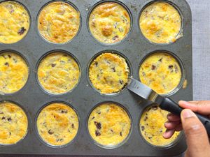Muffin tin with cooked bacon and egg bites, hand using knife to remove one