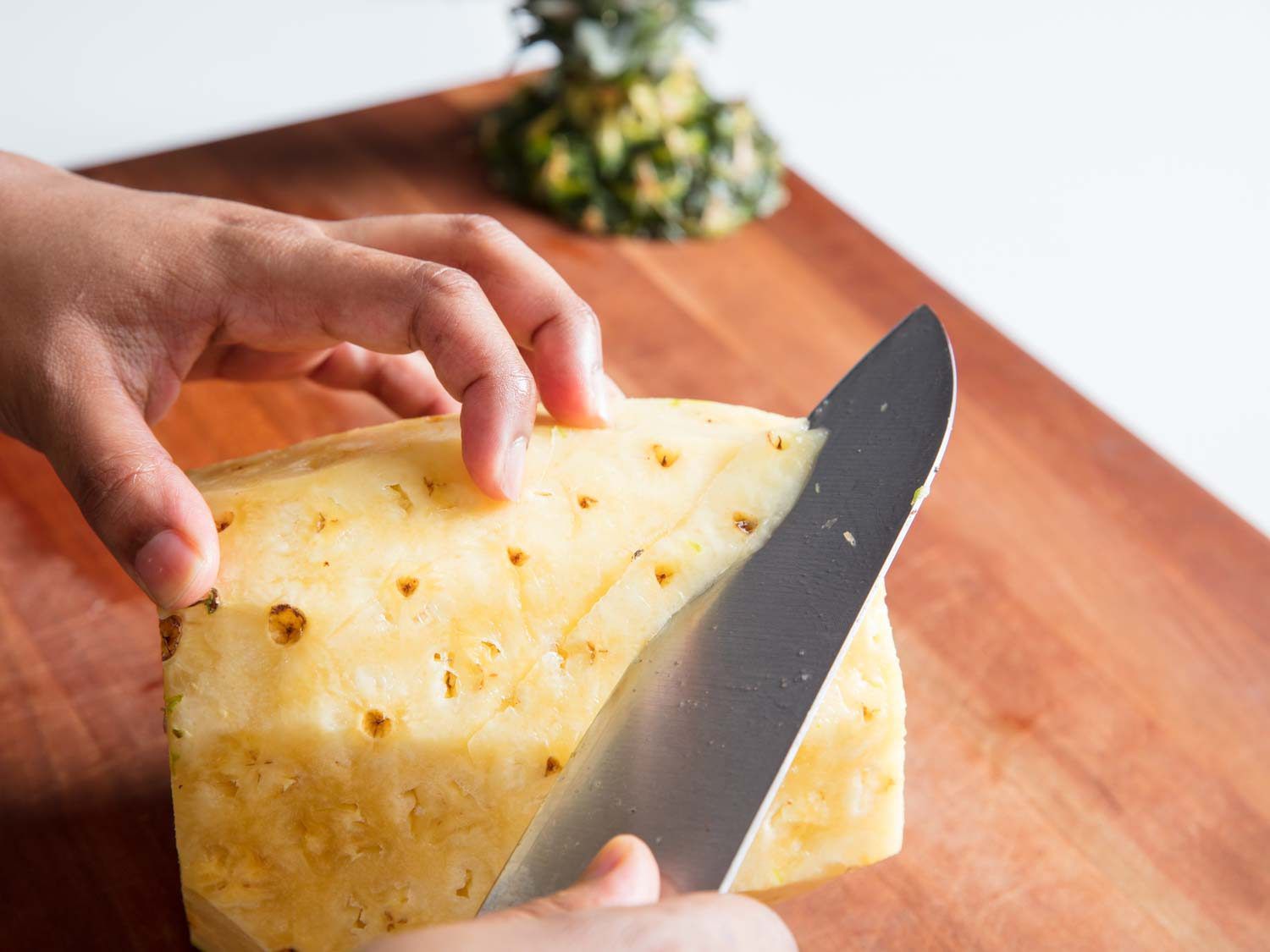 A knife cutting diagonally along the eyes of a pineapple.