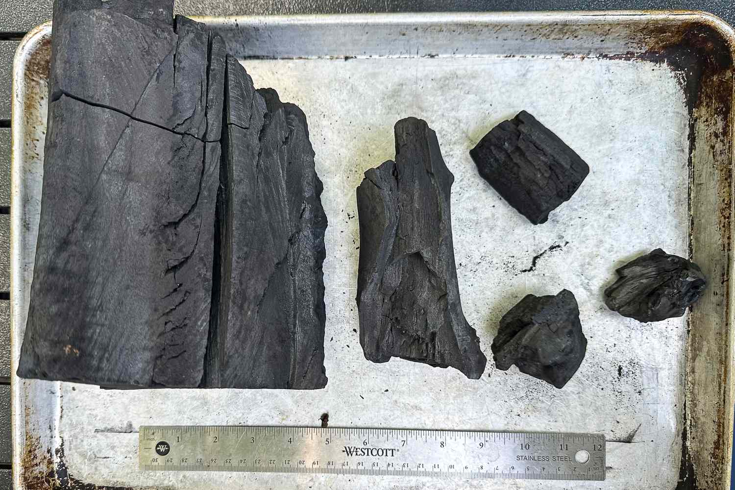 Five different sizes of lump charcoal on a rimmed sheet pan