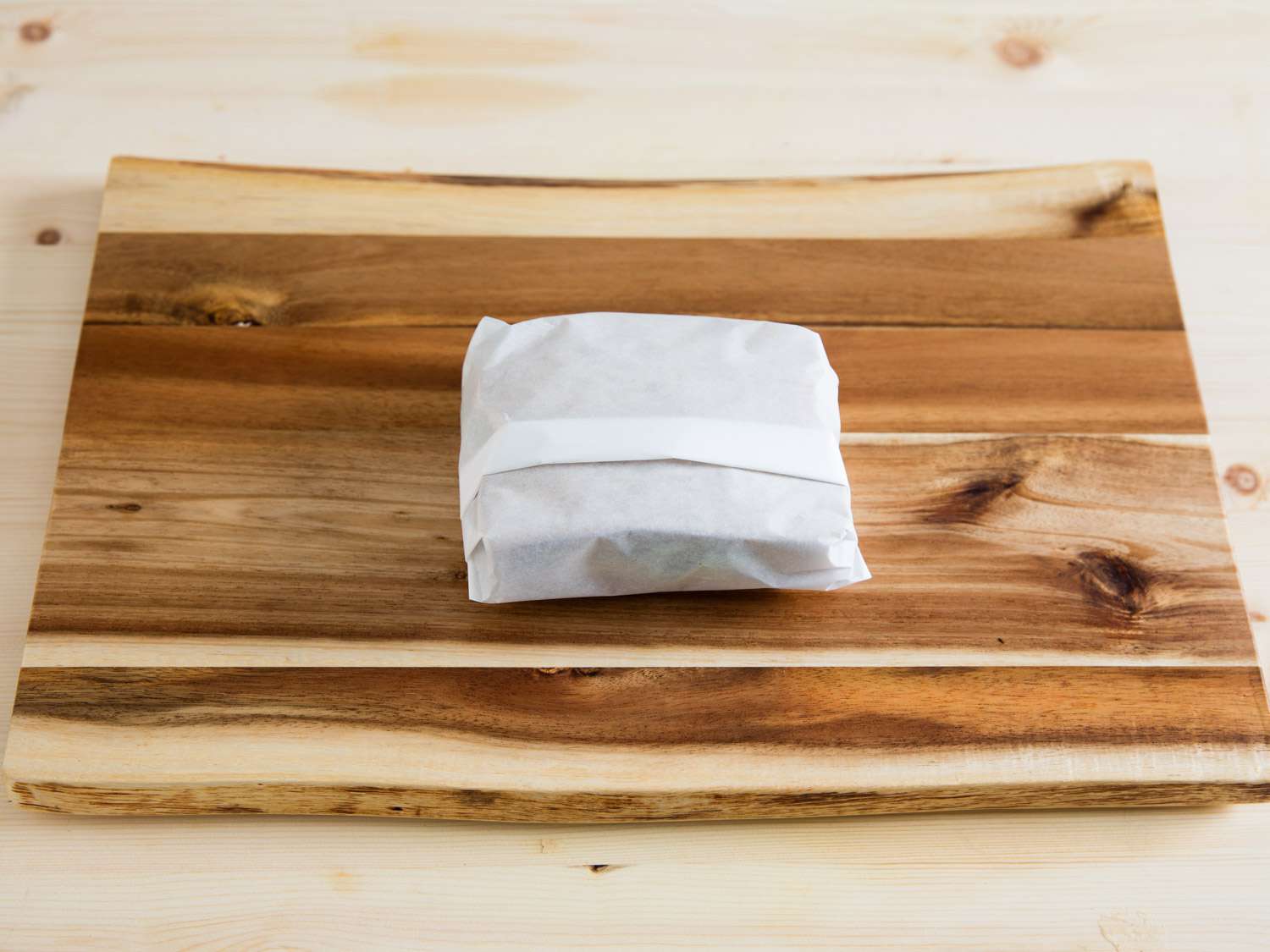 A sandwich wrapped in paper, on top of a cutting board.