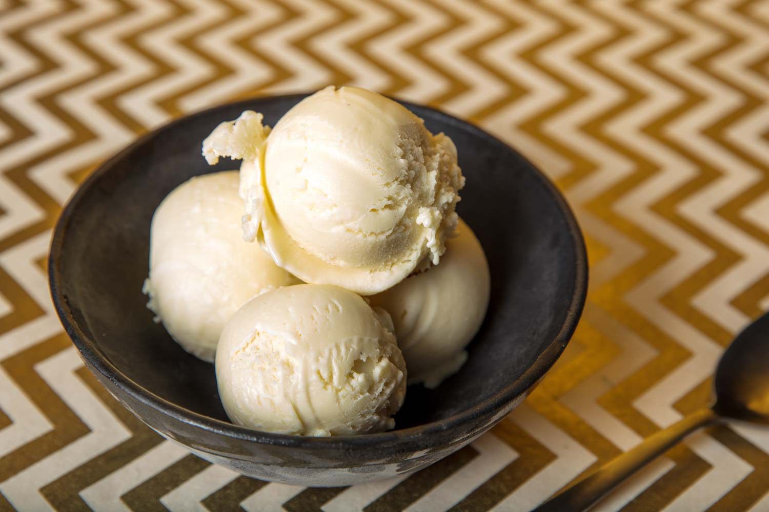 Four scoops of buttermilk ice cream in a black bowl.