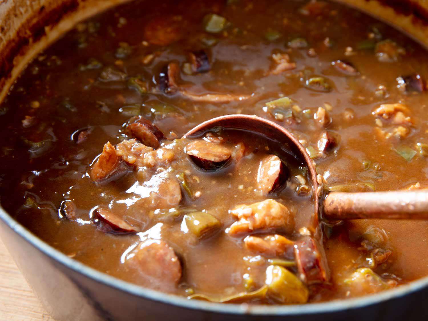 A ladle collecting a spoonful of gumbo from the Dutch oven. 