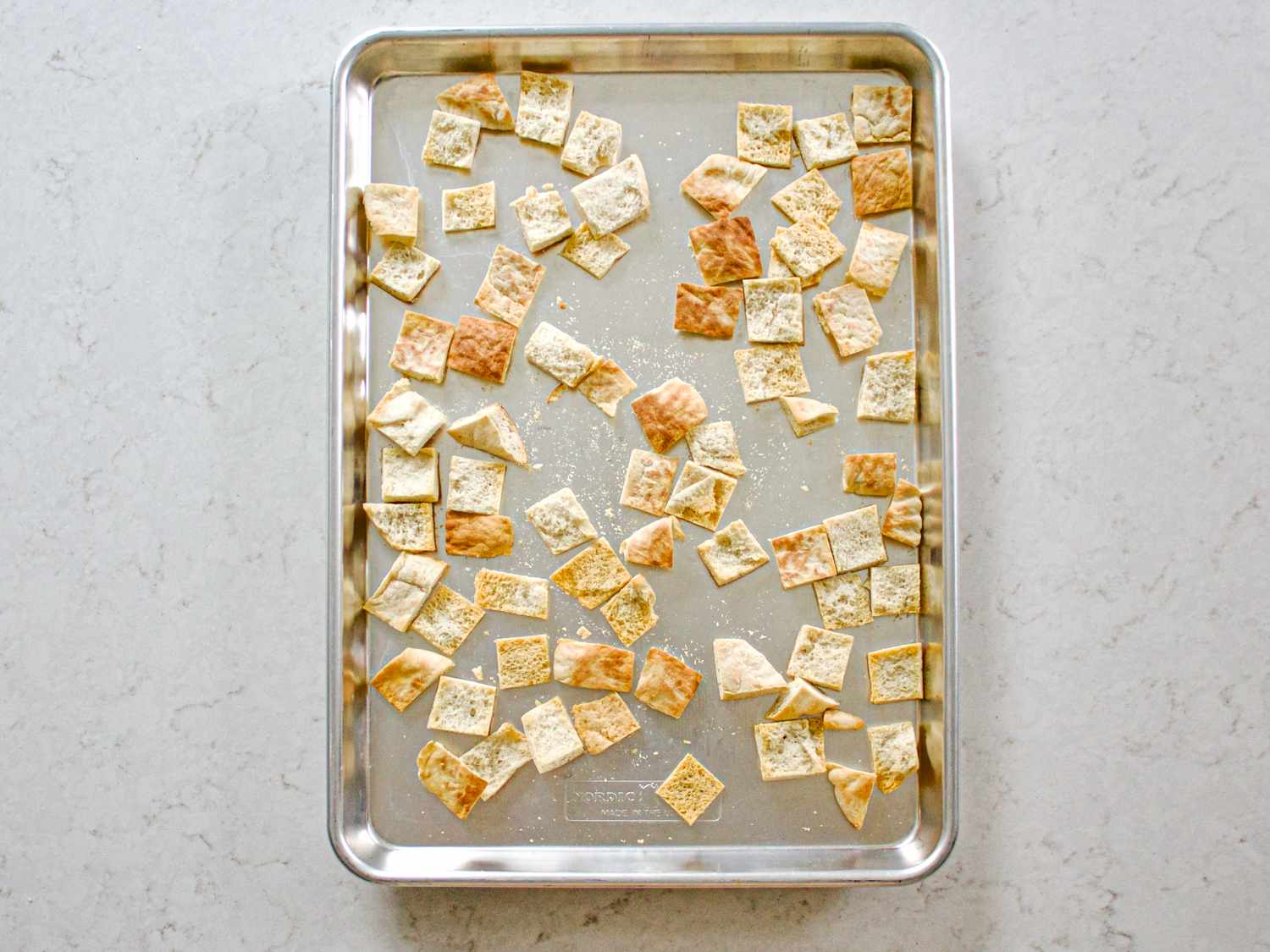 A baking sheet with baked bread pieces spread out evenly