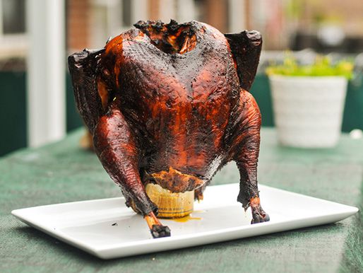 Whole smoked turkey propped vertically on a beer can on a serving platter