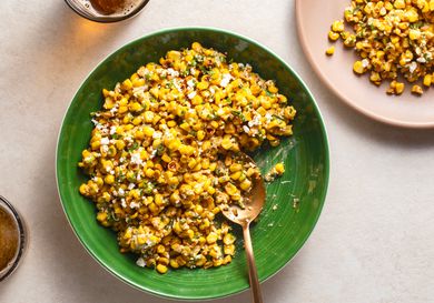 Esquites in a green ceramic bowl with a serving spoon