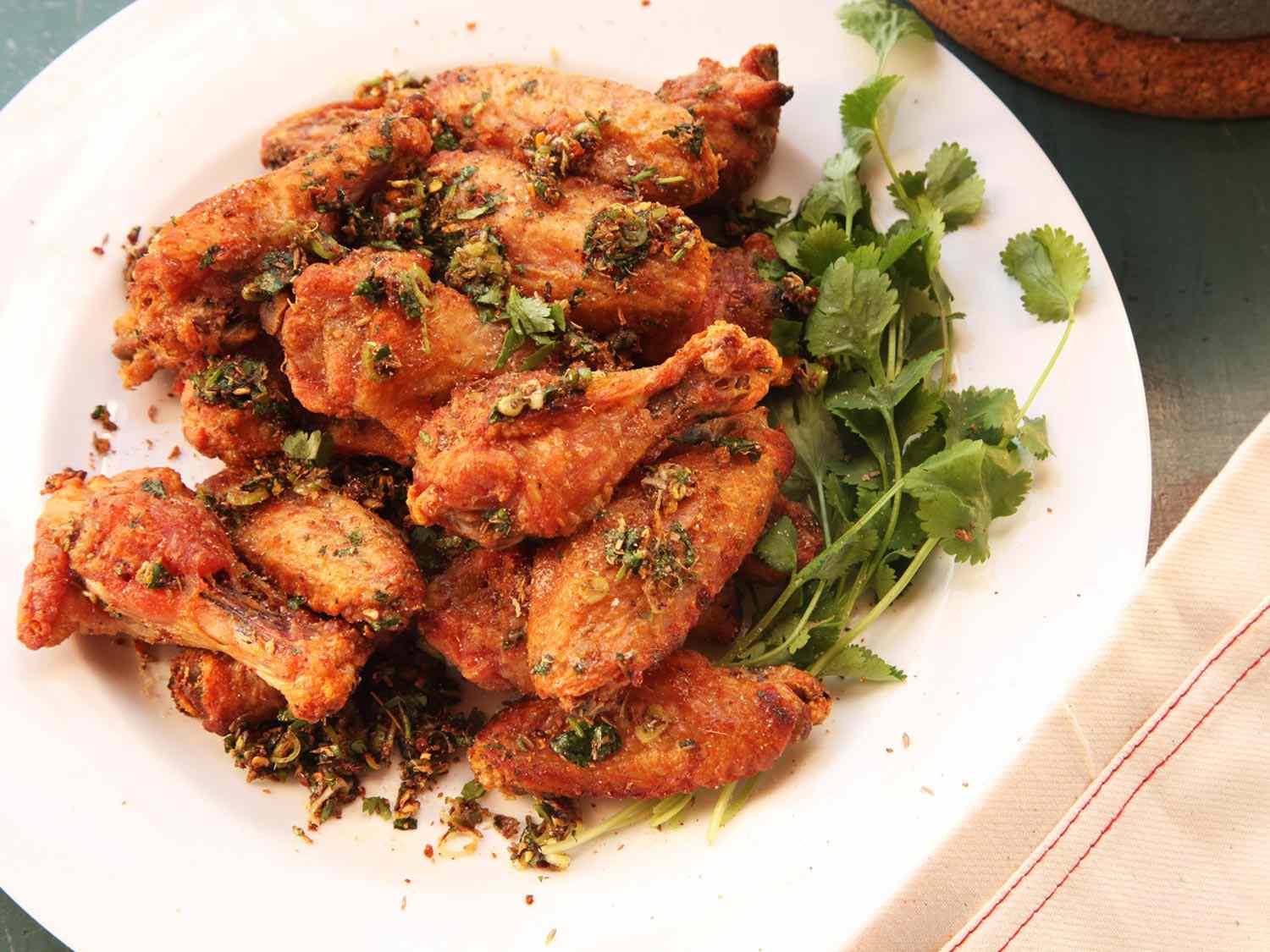 A round porcelain plate holding a pile of hot and numbing chicken wings with some cilantro sprigs.