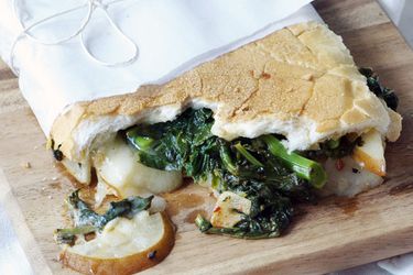Closeup of a half-eaten Broccoli Rabe, Pear, and Fontina Sandwich. The sandwich has been wrapped in a wax paper "diaper."