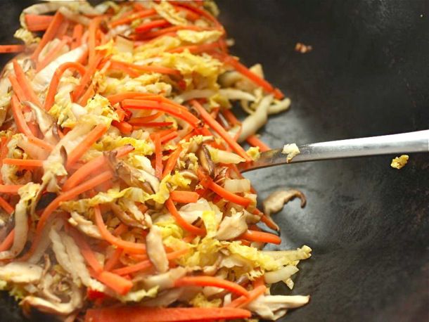 Closeup of the carrot, cabbage, and mushrooms being stir-fried in a wok.