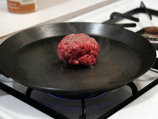 A ball of seasoned ground beef on a smoking hot carbon steel skillet before being smashed into a burger patty.