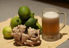 Stein of ginger beer displayed on straw mat with fresh ginger and limes