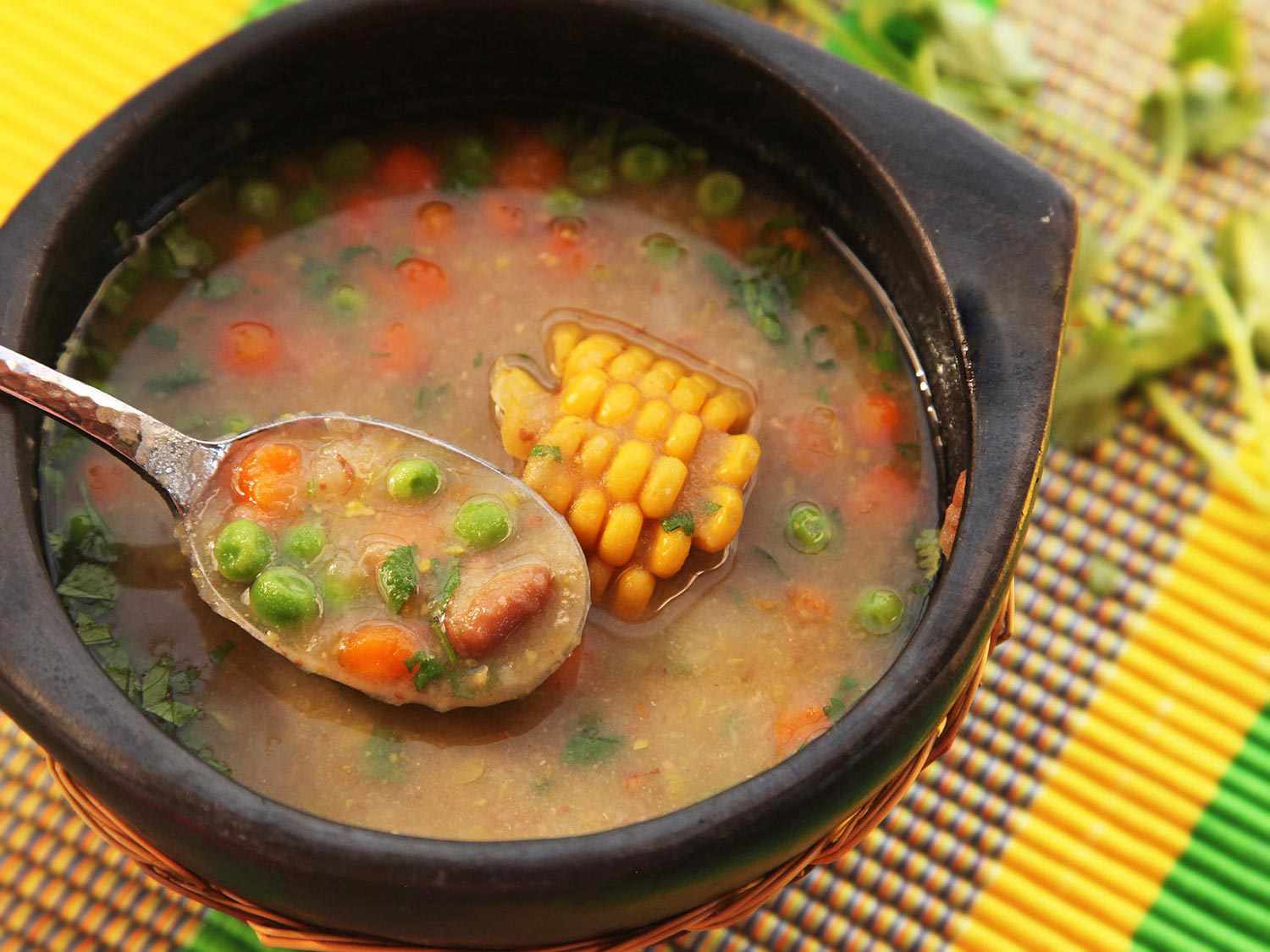 A bowl of ajiaco negro. A spoon raises a bite from the bowl.