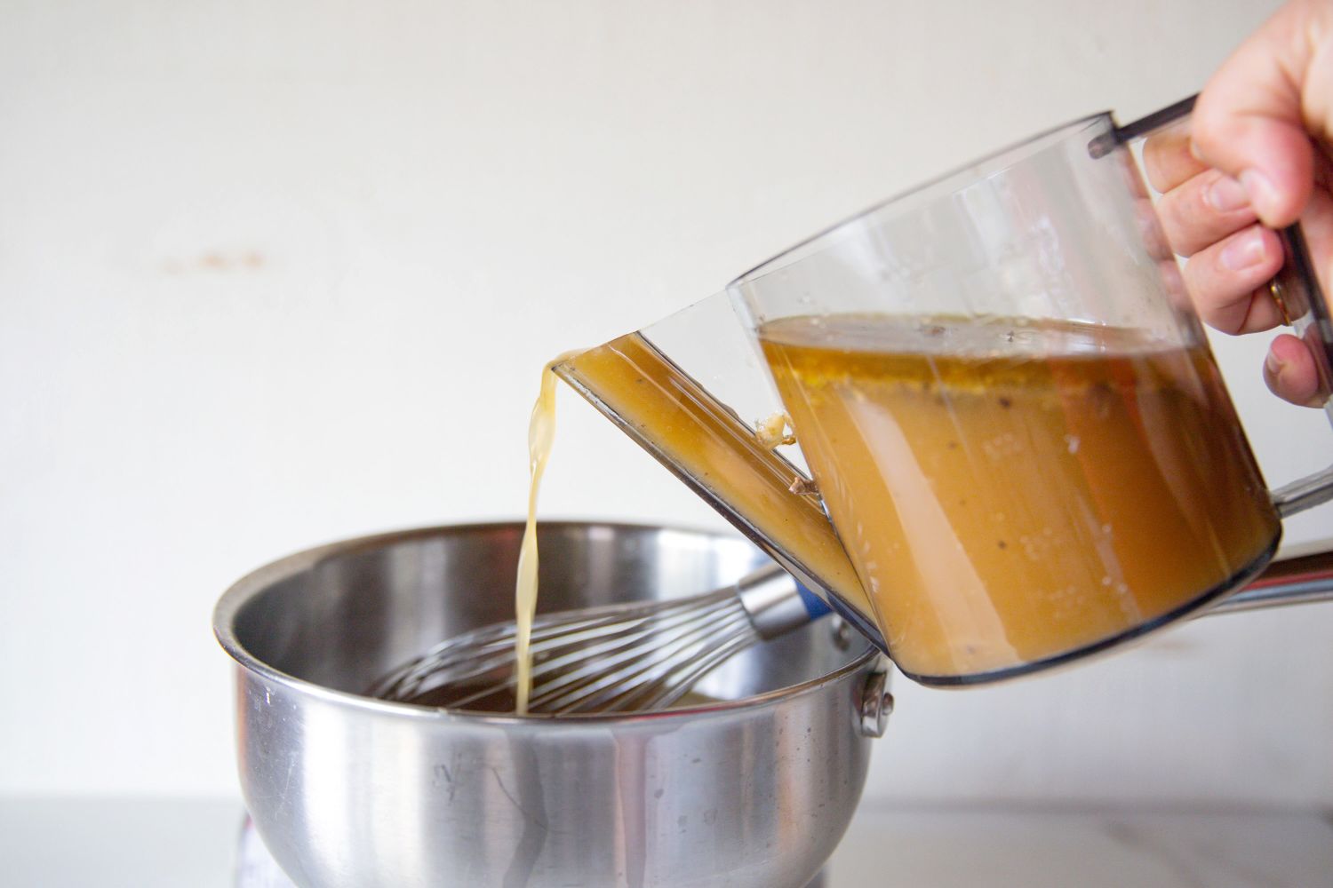 Liquid being poured into a metal bowl containing a whisk